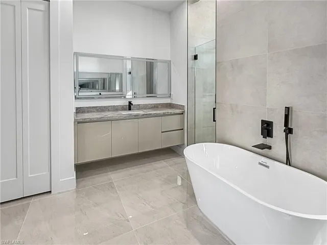Full bathroom with vanity, a soaking tub, tile walls, and a stall shower