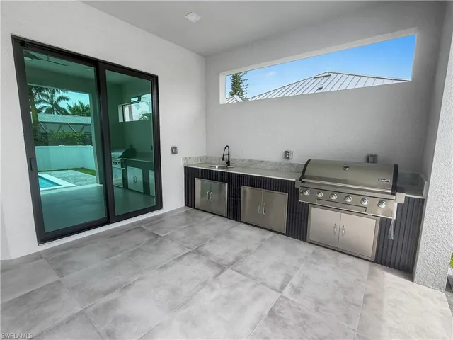 Outdoor kitchen featuring a built-in grill, integrated sink with matte black faucet, and stone countertops
