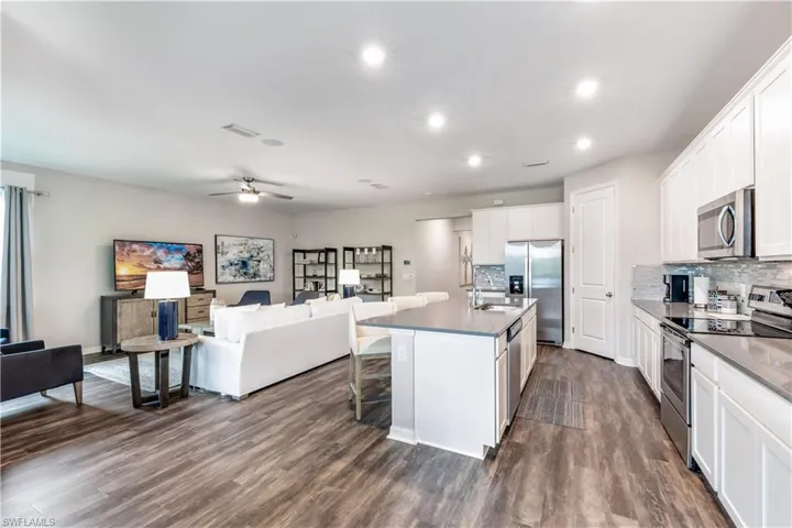 Kitchen featuring ceiling fan, stainless steel appliances, white cabinets, an island with sink, and dark hardwood / wood-style floors