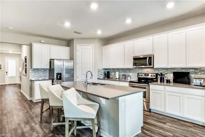 Kitchen with white cabinets, a kitchen island with sink, dark hardwood / wood-style floors, stainless steel appliances, and sink