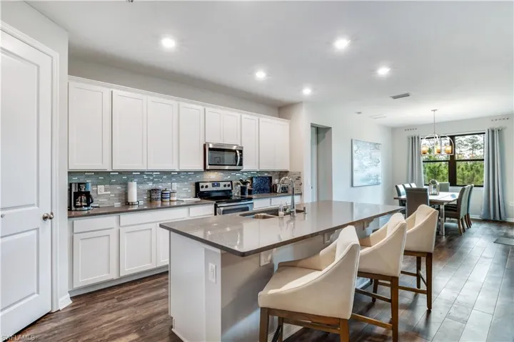 Kitchen with white cabinetry, dark wood-type flooring, a kitchen island with sink, stainless steel appliances, and pendant lighting