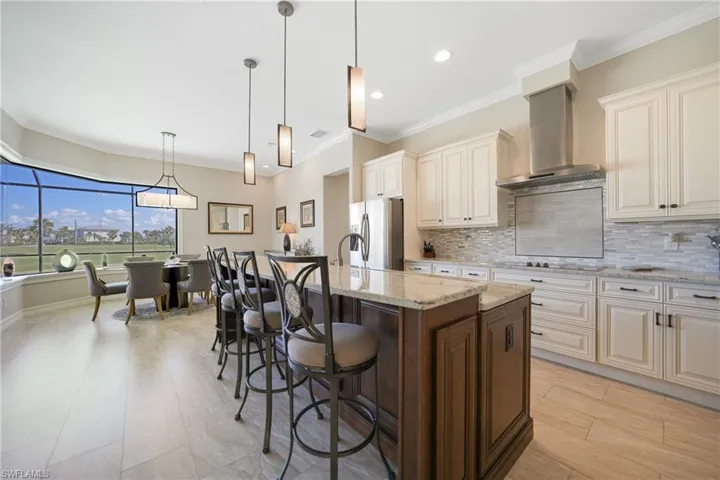 Kitchen featuring stainless steel fridge with ice dispenser, a breakfast bar, light stone countertops, pendant lighting, and wall chimney exhaust hood