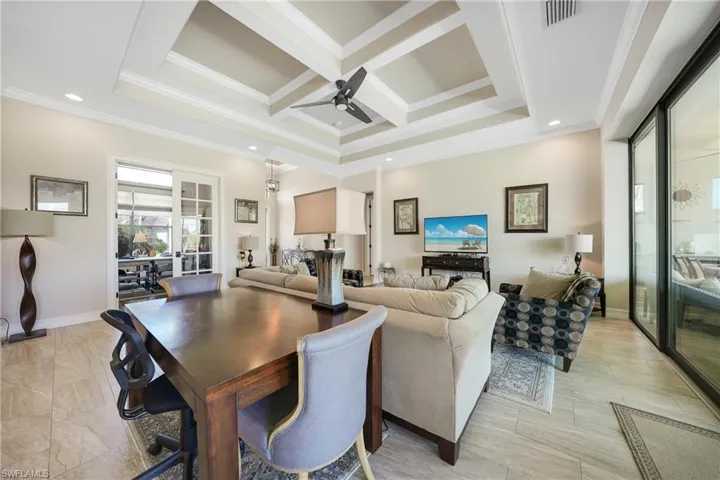 Living room with crown molding, beam ceiling, coffered ceiling, and ceiling fan