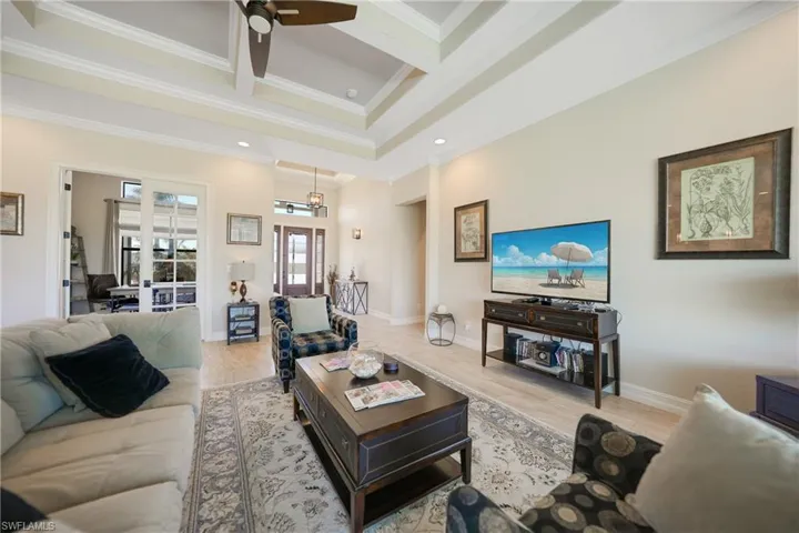 Living room featuring coffered ceiling, crown molding, light hardwood / wood-style floors, and ceiling fan