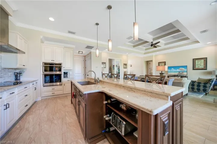 Kitchen with a large island with sink, tasteful backsplash, sink, stainless steel double oven, and wall chimney exhaust hood