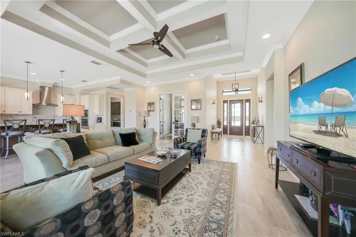 Living room with crown molding, coffered ceiling, beamed ceiling, and ceiling fan with notable chandelier
