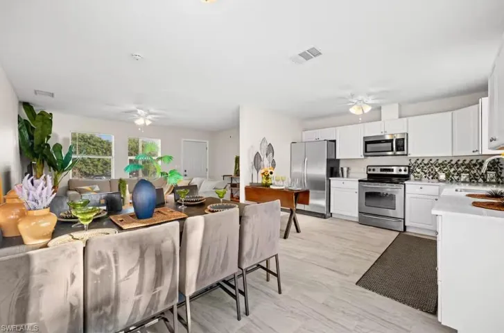 Kitchen featuring ceiling fan, stainless steel appliances, white cabinets, open floor plan, and decorative backsplash
