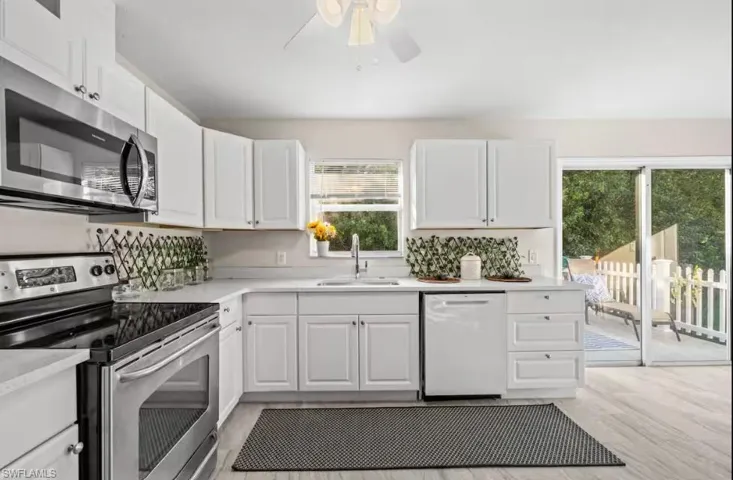 Kitchen with stainless steel appliances, a ceiling fan, white cabinets, and light wood finished floors
