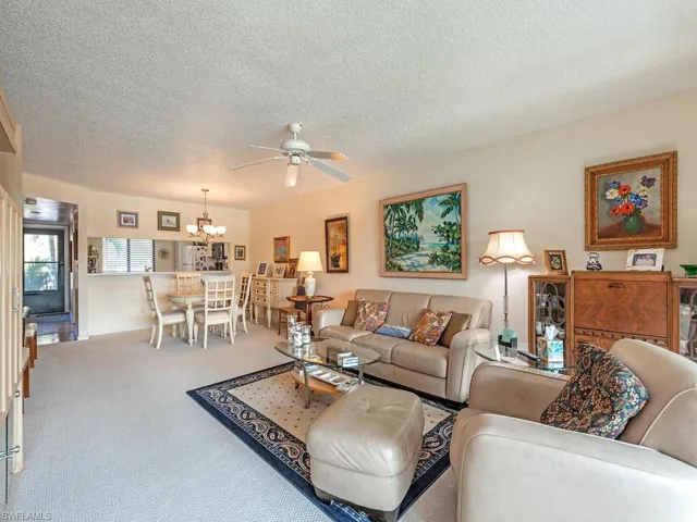 Living room with carpet floors, a textured ceiling, and ceiling fan with notable chandelier