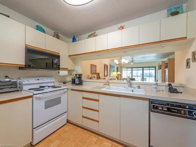 Kitchen featuring light countertops, white cabinets, a sink, a textured ceiling, and white appliances