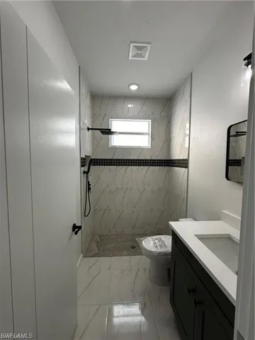 Bathroom with tiled shower, vanity, and toilet