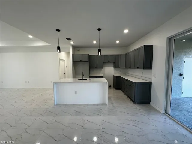 Kitchen with gray cabinetry, hanging light fixtures, sink, and an island with sink
