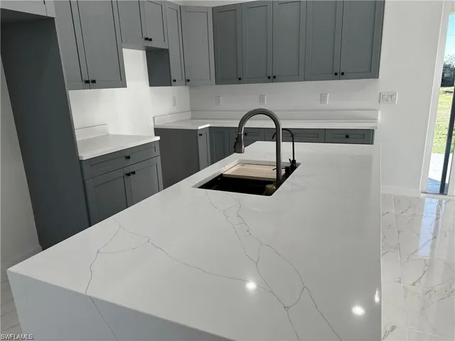 Kitchen featuring gray cabinets, sink, and light stone counters