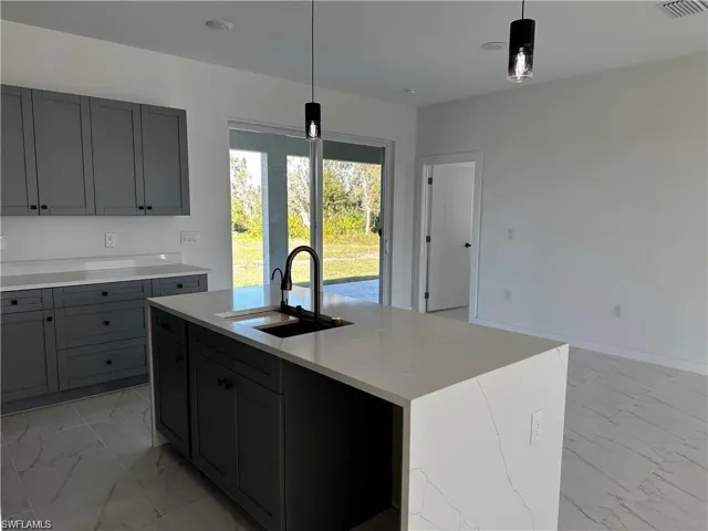 Kitchen with sink, a kitchen island with sink, light stone counters, and decorative light fixtures