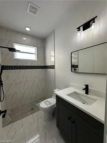 Bathroom featuring vanity, toilet, and a tile shower