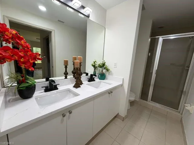 Bathroom with double vanity, a shower stall, and light tile patterned flooring