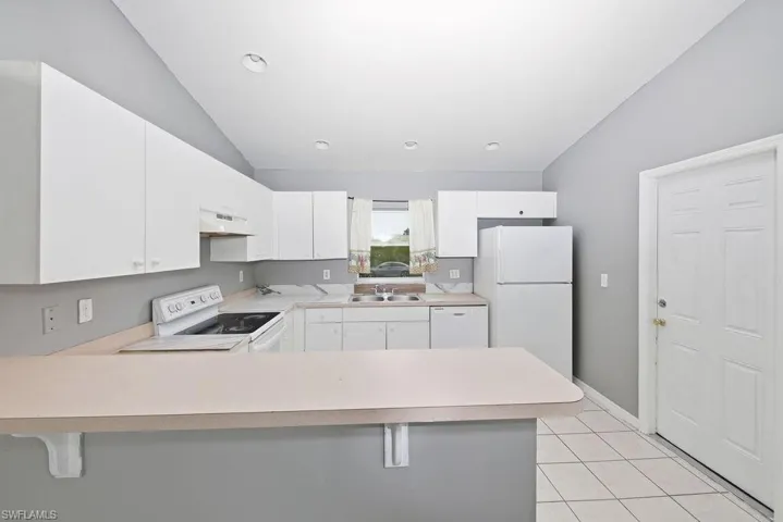 Kitchen featuring white cabinetry, light countertops, integrated dual basin sink, white tile flooring, and a breakfast bar