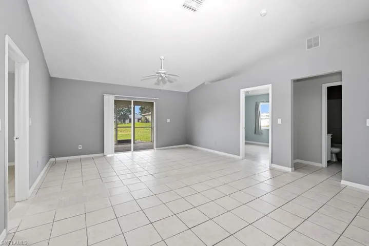 Spacious room featuring vaulted ceilings, light tile flooring, and neutral gray walls