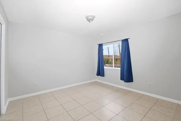 Bright interior space featuring neutral wall paint, square tile flooring, and a single window with white trim