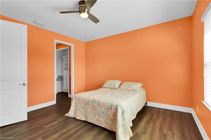 Bedroom with a spacious closet, dark wood-type flooring, a ceiling fan, and multiple windows