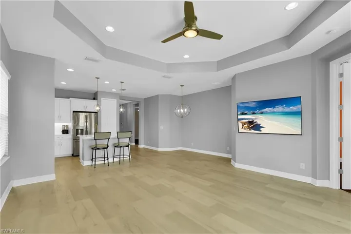 Unfurnished living room with a chandelier, a tray ceiling, light wood-type flooring, ceiling fan, and recessed lighting