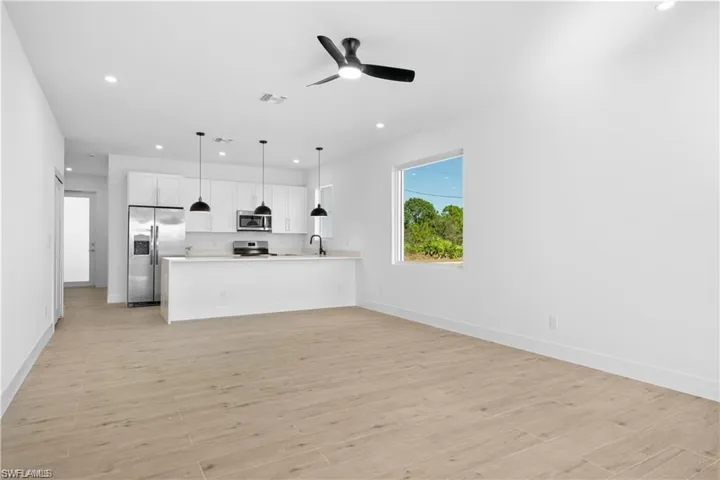 Kitchen with appliances with stainless steel finishes, white cabinetry, sink, hanging light fixtures, and light wood-type flooring