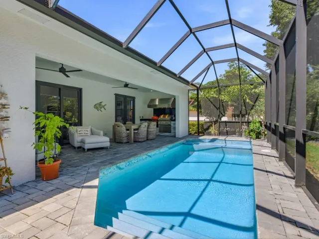 Screened-in outdoor patio featuring a rectangular swimming pool with integrated steps, stone-paver decking, built-in outdoor kitchen with a stainless steel grill, and dual ceiling fans