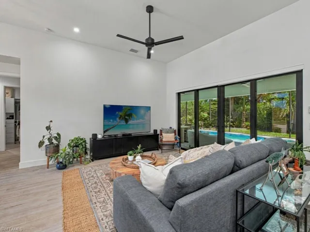 High-vaulted ceilings featuring a matte black ceiling fan, wood-finish flooring, and expansive multi-panel sliding glass doors providing outdoor access