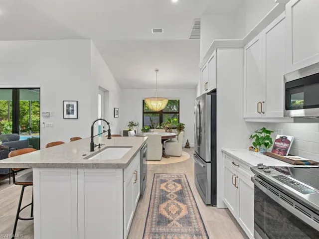 Kitchen featuring white cabinetry, stone-finish countertops, a central island with an integrated sink, stainless steel appliances, and wood-finish flooring