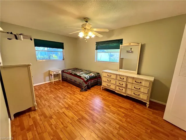 Bedroom with laminate / wood-style flooring, multiple windows, a textured ceiling, and ceiling fan