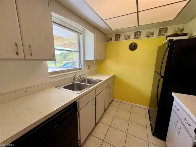 Kitchen featuring black appliances, sink, white cabinetry, and light tile floors