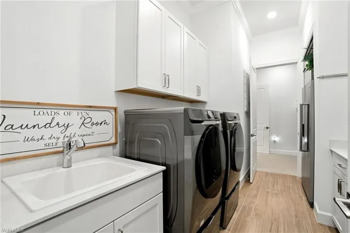 Laundry area featuring light wood-type flooring, ornamental molding, washer and clothes dryer, and cabinet space