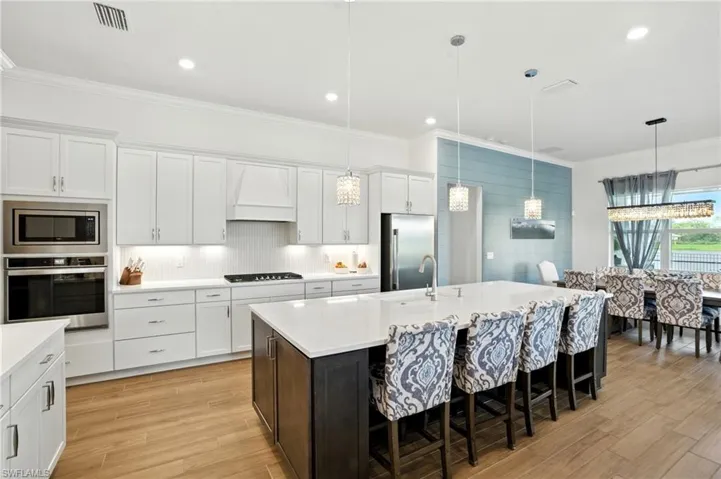 Kitchen featuring crown molding, white cabinetry, a kitchen bar, stainless steel appliances, and an island with sink