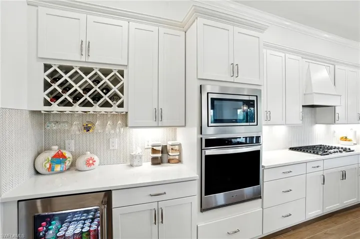 Kitchen with wine cooler, tasteful backsplash, stainless steel appliances, white cabinets, and ornamental molding