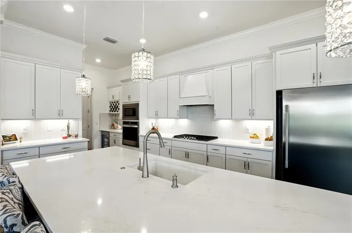 Kitchen featuring ornamental molding, pendant lighting, tasteful backsplash, stainless steel appliances, and premium range hood
