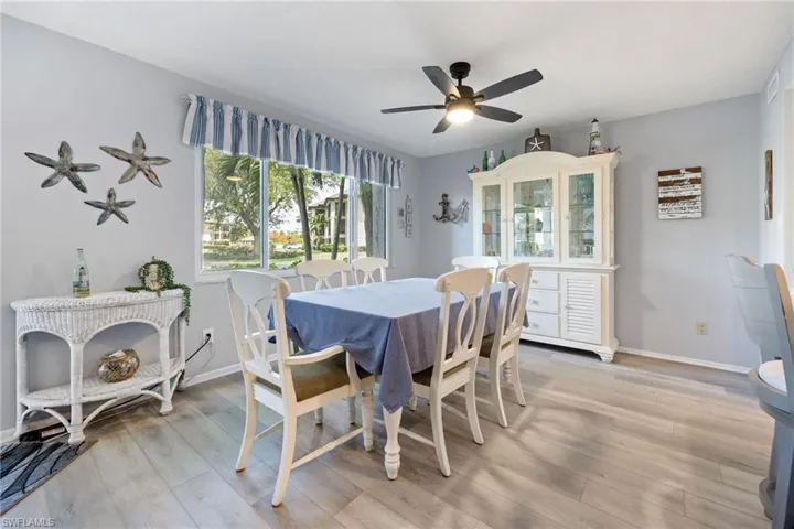 Dining area featuring light-toned wood-finish flooring, a contemporary ceiling fan with integrated lighting, and multiple windows providing ample natural light