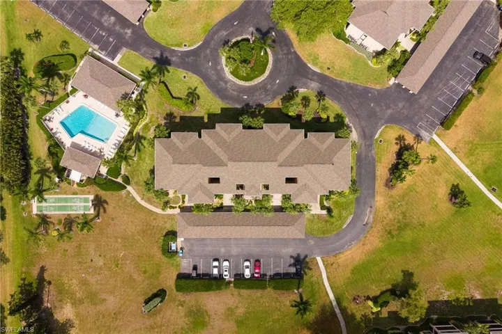 Aerial panorama showcasing the property's main building, swimming pool, two bocce ball courts, and surrounding paved roadways