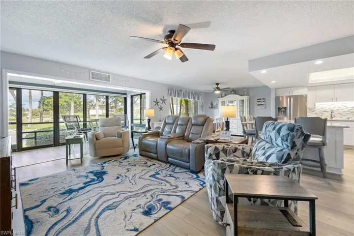 Spacious open-concept living area featuring light wood-finish flooring, a large area rug, and a ceiling fan