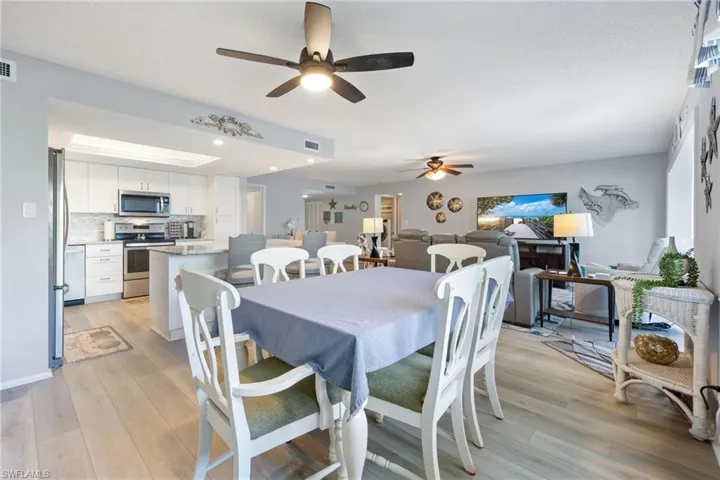 Open-concept living area featuring wood-finish flooring throughout, a kitchen with white cabinetry and stainless steel appliances, and ceiling fans