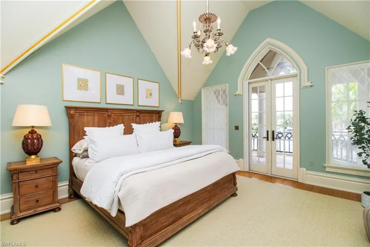 Bedroom featuring a notable chandelier, french doors, access to exterior, hardwood / wood-style floors, and high vaulted ceiling