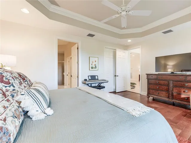 Bedroom featuring recessed lighting, crown molding, ensuite bath, a tray ceiling, and dark wood flooring