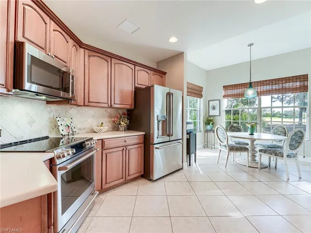 Kitchen featuring appliances with stainless steel finishes, decorative light fixtures, brown cabinets, tasteful backsplash, and light tile patterned floors