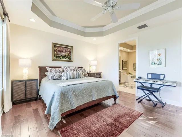 Bedroom featuring a raised ceiling, light wood-type flooring, ornamental molding, ceiling fan, and ensuite bathroom