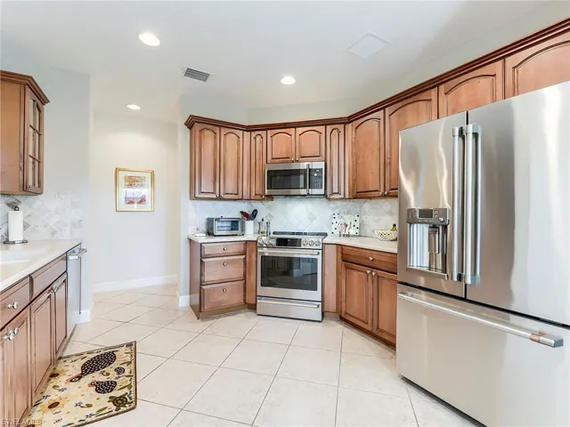 Kitchen featuring stainless steel appliances, brown cabinetry, light tile patterned floors, recessed lighting, and tasteful backsplash