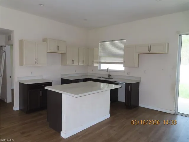 Kitchen featuring light countertops, dark wood-type flooring, dual tone cabinetry, a center island, and stainless steel dishwasher