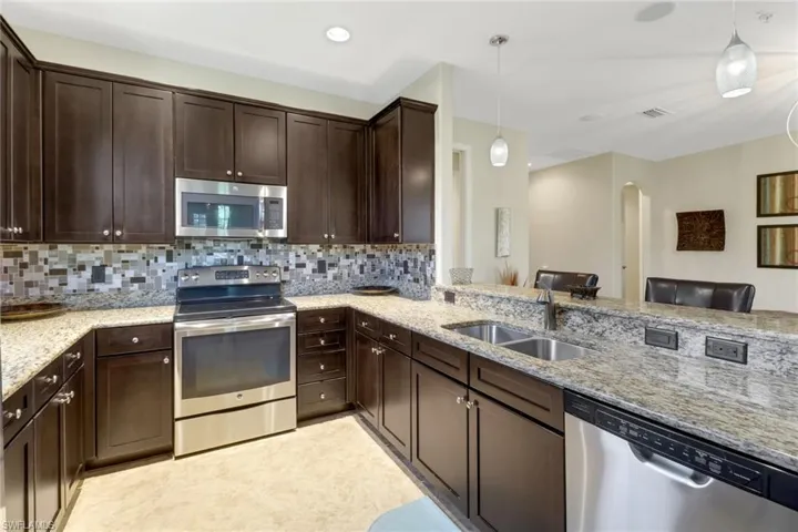 Kitchen with hanging light fixtures, sink, appliances with stainless steel finishes, and tasteful backsplash