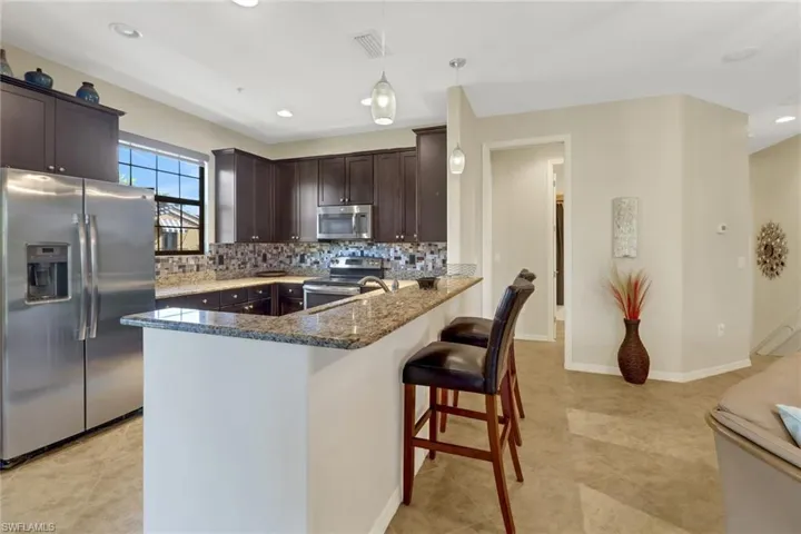 Kitchen with kitchen peninsula, appliances with stainless steel finishes, tasteful backsplash, decorative light fixtures, and a breakfast bar area