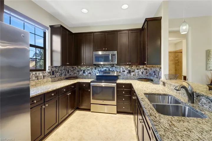 Kitchen featuring pendant lighting, sink, light stone countertops, and stainless steel appliances