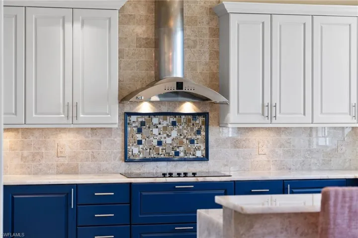Kitchen featuring blue cabinets, wall chimney range hood, white cabinetry, and backsplash
