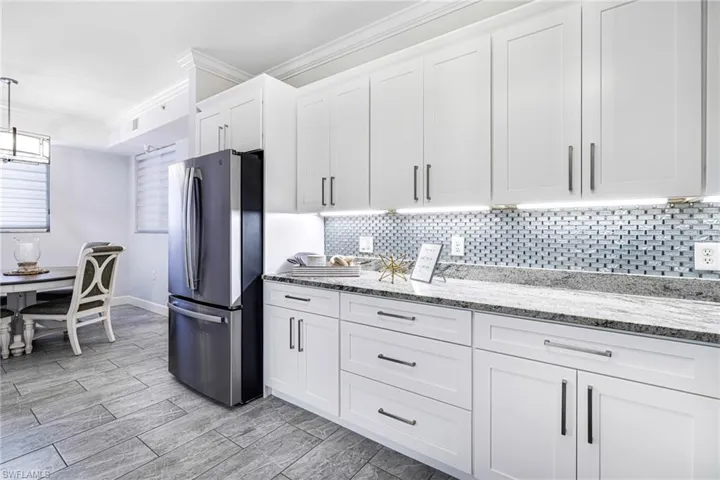 Kitchen with light stone countertops, stainless steel fridge, tasteful backsplash, crown molding, and white cabinetry